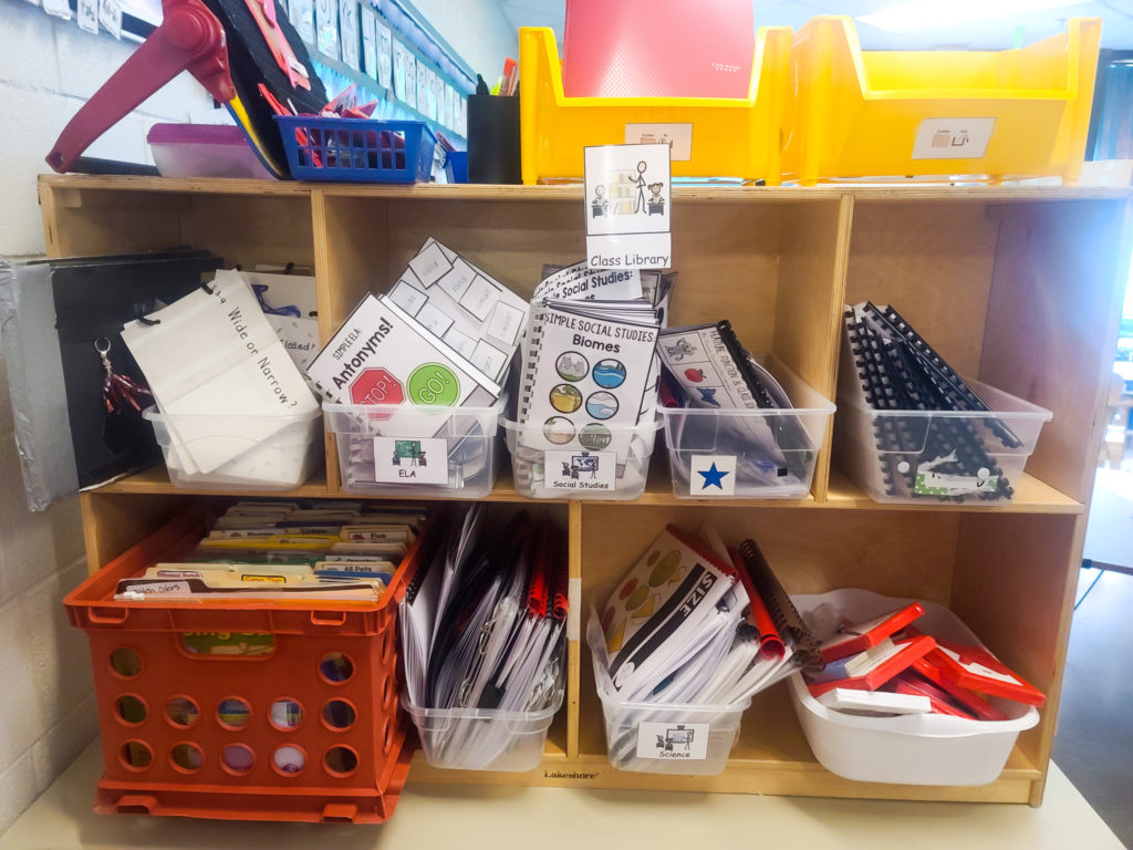 A wooden shelf with containers filled with adapted books.