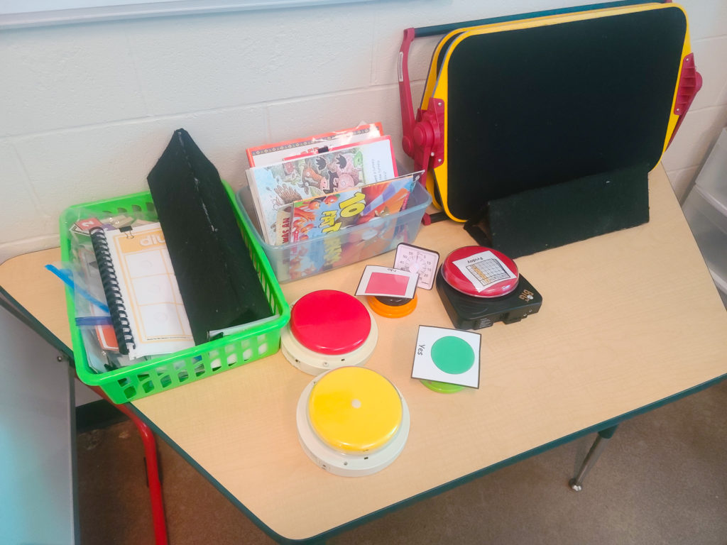 Green basket with laminated education activities, 5 switches, a timer, and 3 velcro boards.