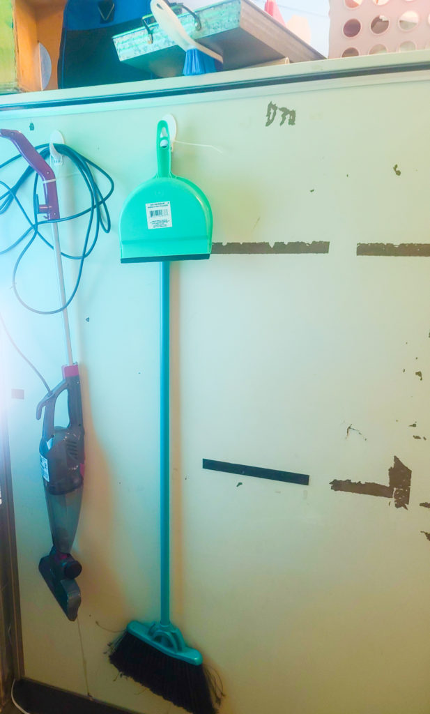 Broom and vacuum hanging on the back of a cabinet.