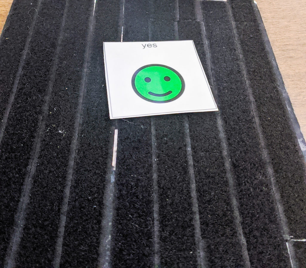 Black velcro board with a green smiley face card on it.