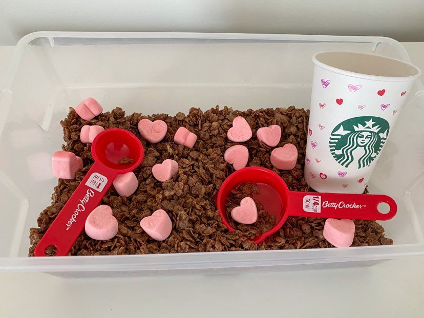Valentine's Day Sensory bin with cocoa flakes and marshmallow hearts with 1/4 cup scoops and a Starbucks up with hearts on it