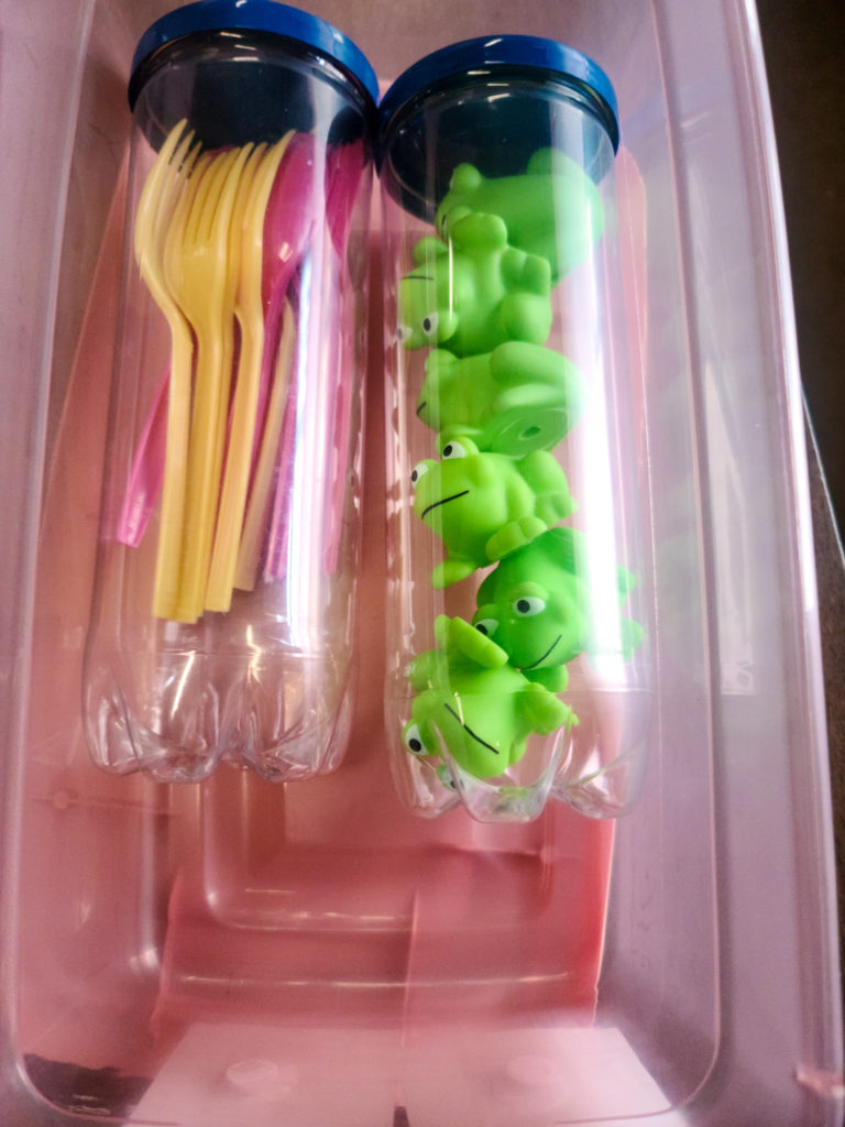 Picture of 2 plastic tubes. One with pink and yellow forks and spoons and one with green bathtub frogs.