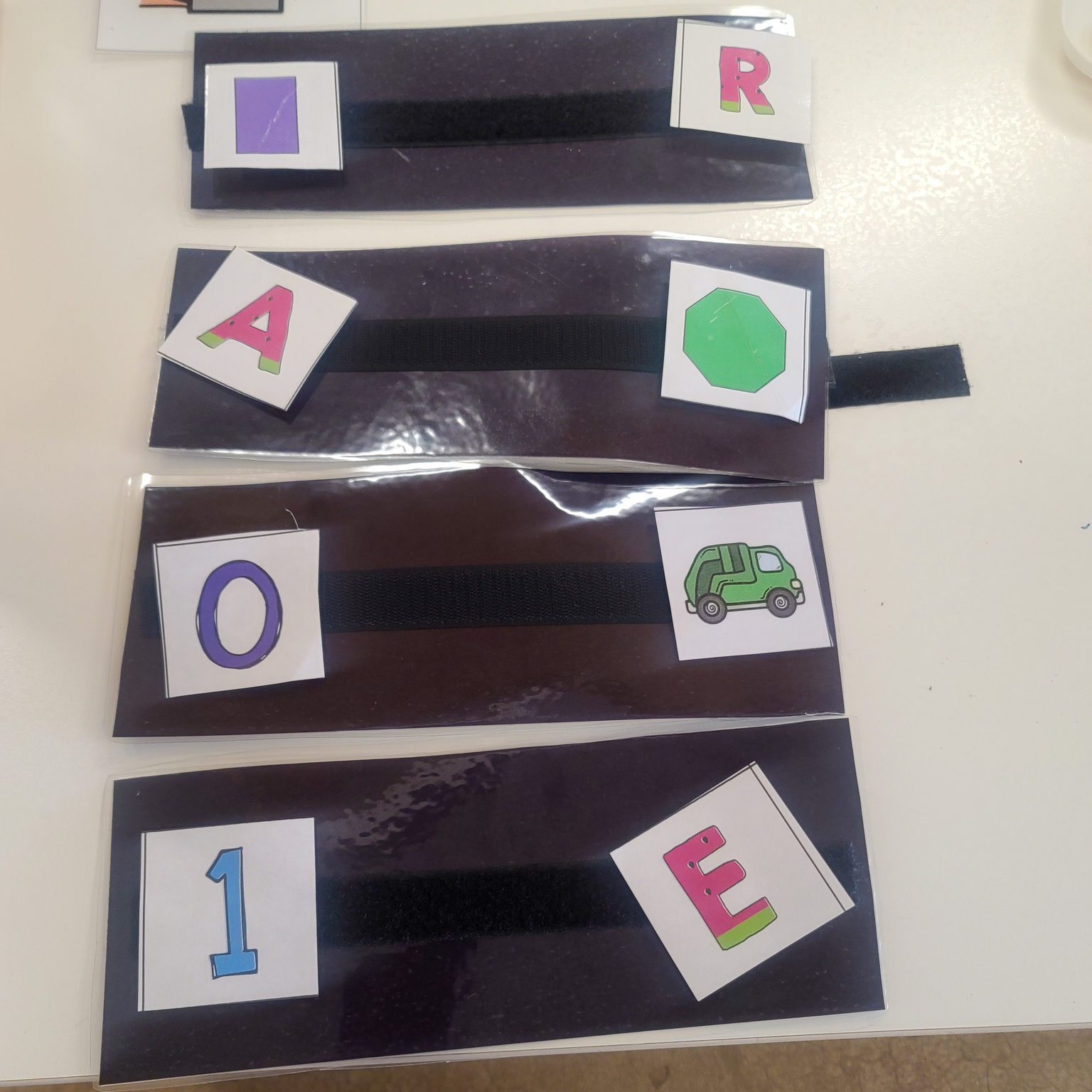 Picture of 4 black strips with letters, shapes, and colors on them.
