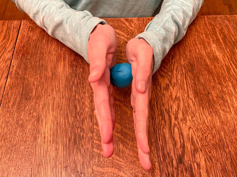 using two hands to roll playdough into a small ball. 
