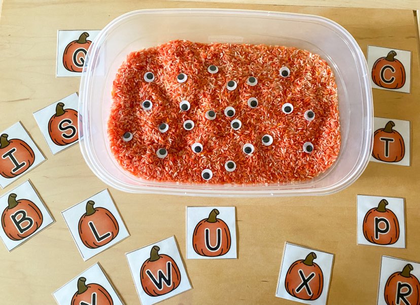sensory bin with orange rice, google eyes and cards featuring pumpkins/uppercase letters