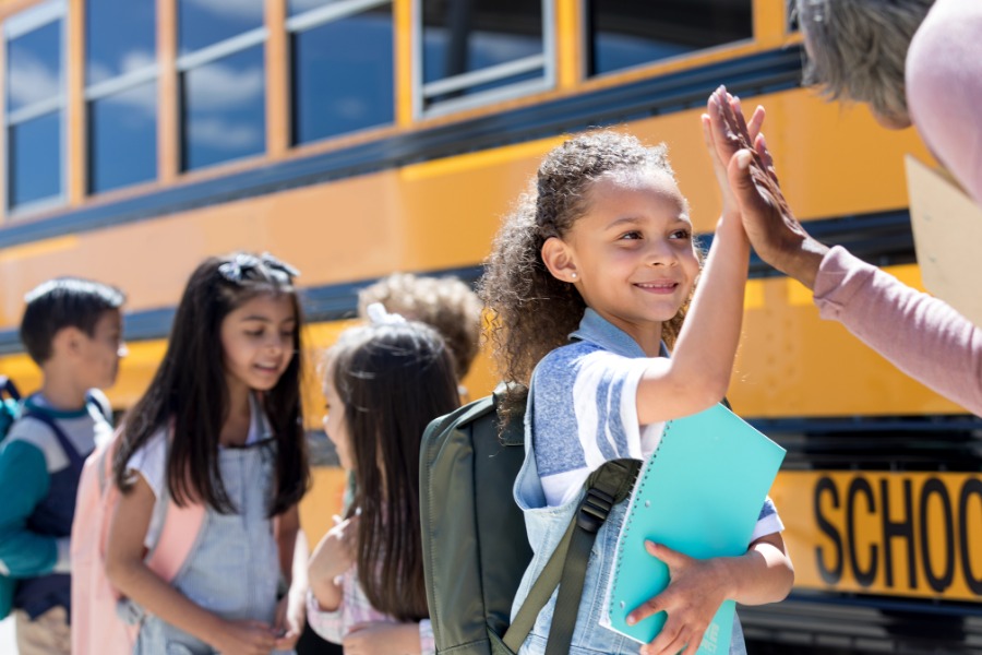 This is a photo of a teacher giving a student a high five by a school bus. 
