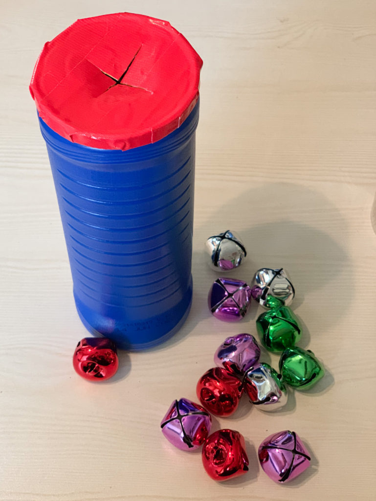 This is a photo of an errorless Christmas task box.  It is an empty plastic chip can with a lid.  The lid has an x slit into it.  Students can place Christmas jingle bells inside.