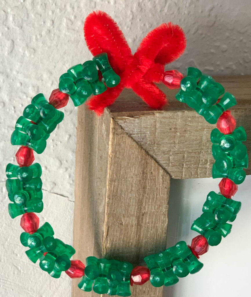 This is a Christmas wreath made out of green and red beads and a red pipe cleaner.