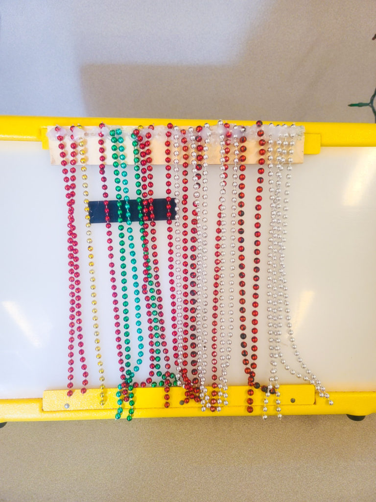  Bead strings hanging from and piece of wood on a light box.
