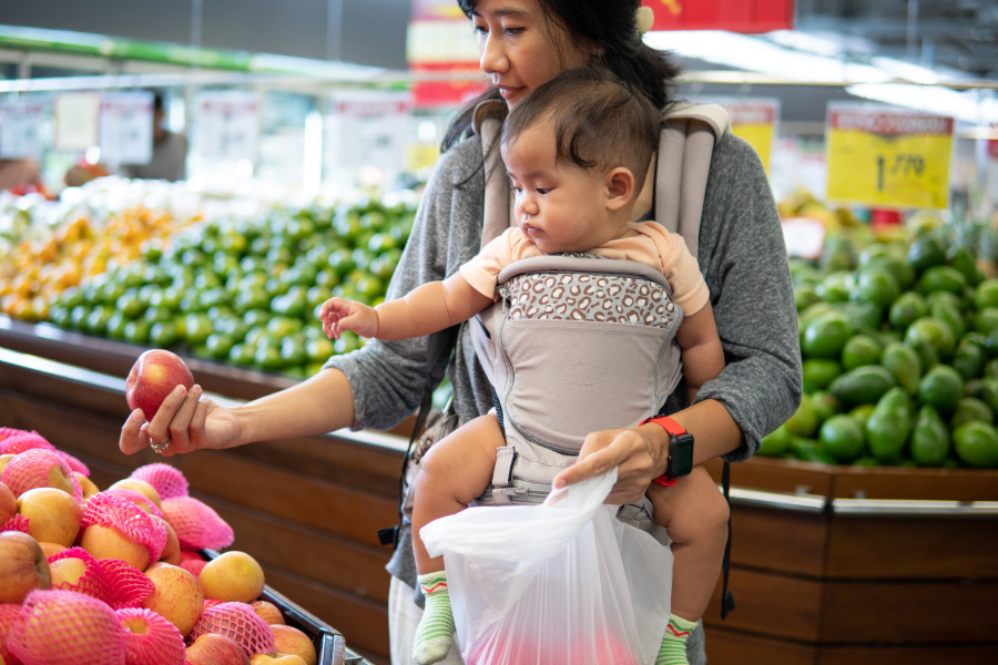 This is an image of a mom grocery shopping with her baby in a baby carrier.