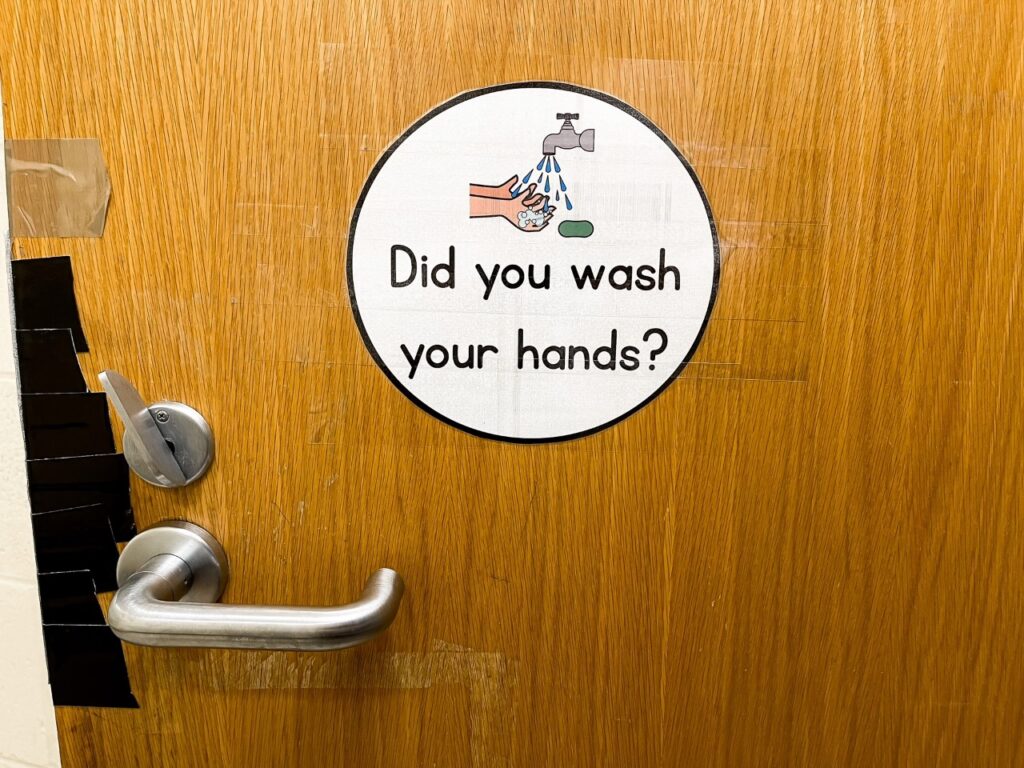 A wooden classroom door with a sign that says "Did you wash your hands?"