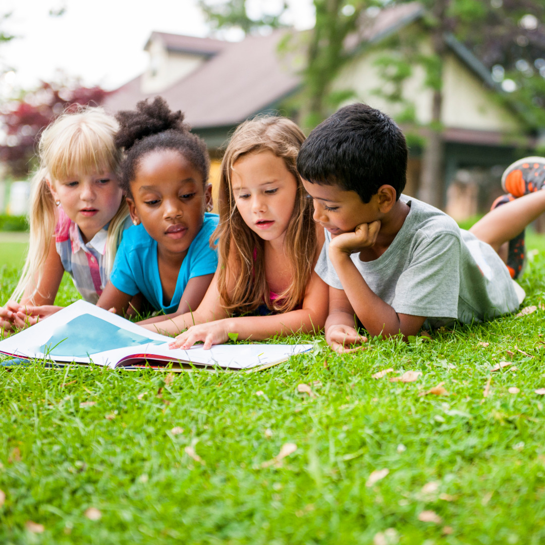 4 children reading a book on the lawn