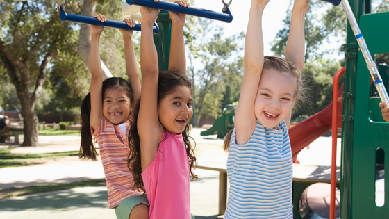 Three young girls hang from the monkey bars