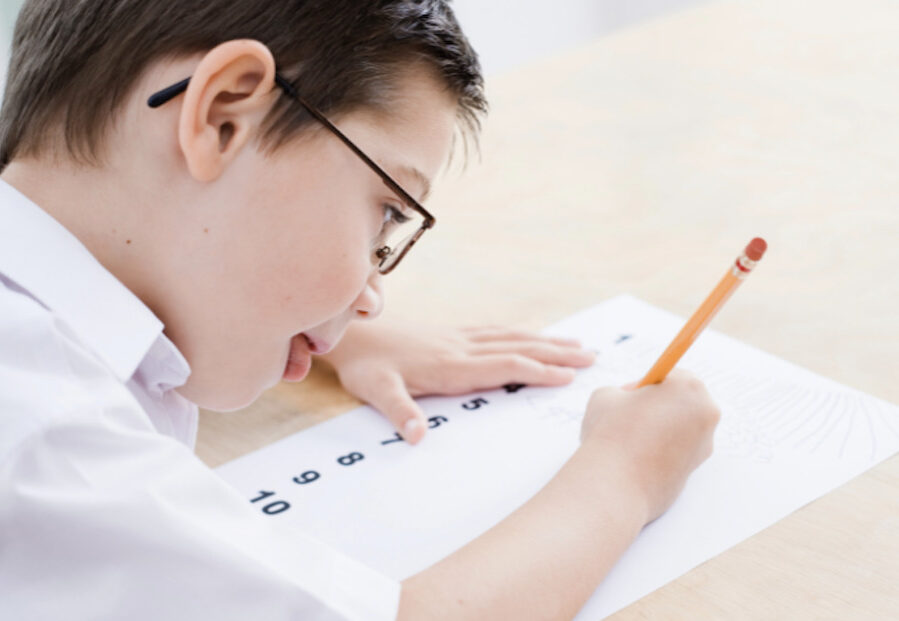 A boy with. Down syndrome writing on a numbers worksheet with a pencil