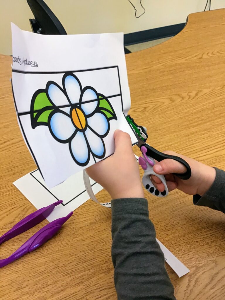 student cutting out a Simply Special Ed cut & paste activity with scissors that have an alligator hungry cutter visual support on them