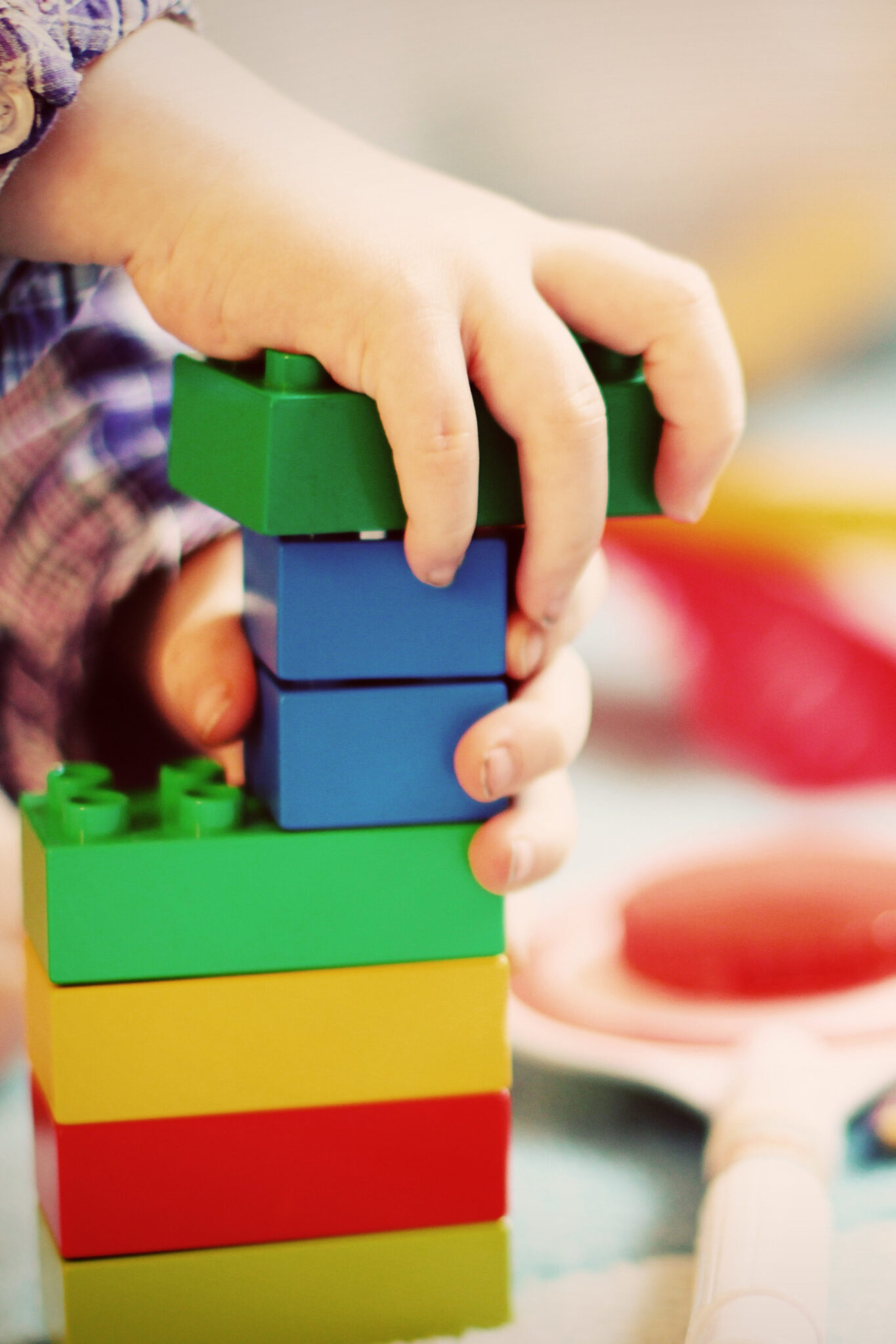 child builds large rainbow colored Lego blocks into a tower