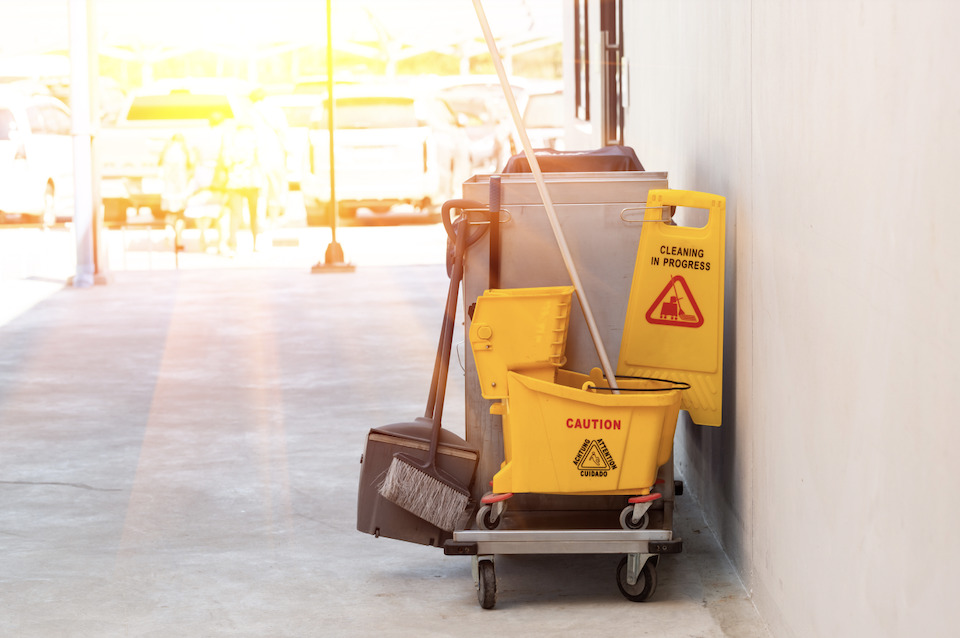 picture of custodial materials like a mop, caution sign and broom on a chart in a sunlit hallway