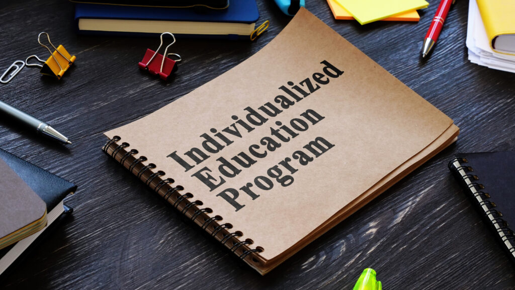 a spiral notebook labeled: "Individuated Education Program" on a messy desk with office supplies