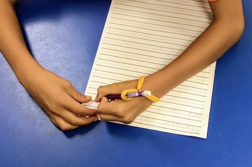 student writes with a mechanical pencil and handy-writer pencil grip on three lined paper