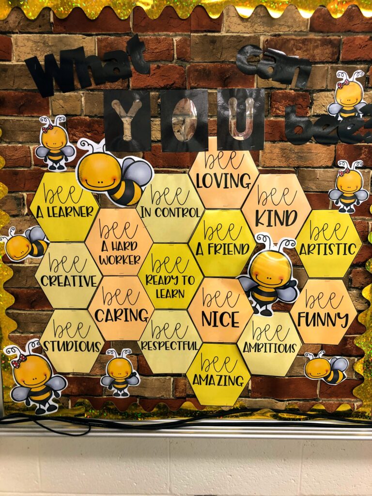 bulletin board with brick background that says "what can you bee?" and has a bee hive with sayings like "bee in control", "bee loving" and "bee a learner", etc.