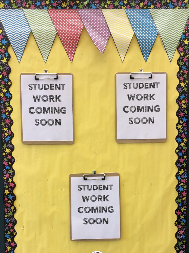 bulletin board with colorful banner and star boarder with 3 clipboard hanging on it that say "student work coming soon"