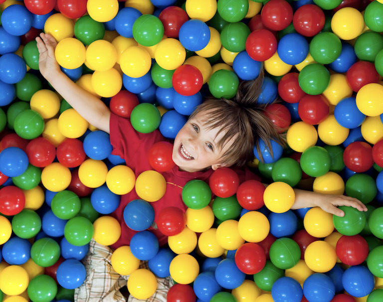student smiling covered by red, blue, yellow and green balls in a ball pit for a tactile sensory experience 