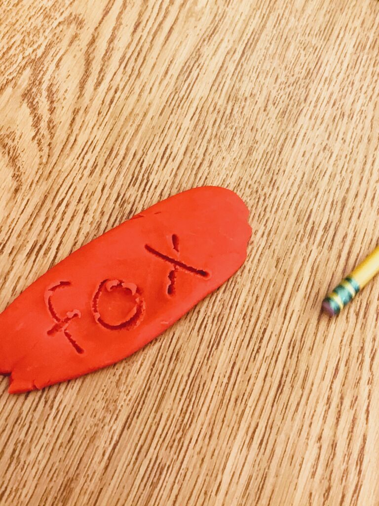 red play dough with "fox" written in it with a pencil as a multi-sensory approach to practice letter formation