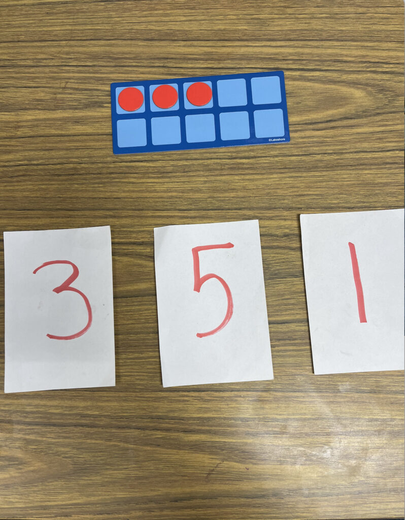 A ten frame withy 3 red dots in the top row with 3 different flashcards reading the numbers 3, 5, & 1.
