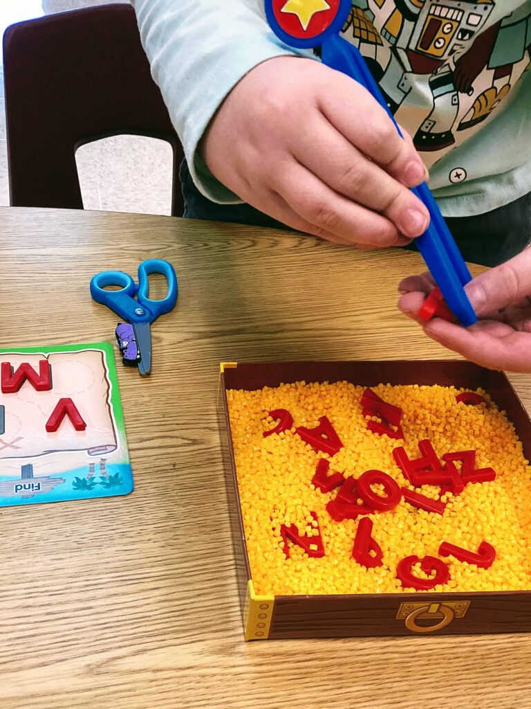 student using tongs to take letters out of a bead sensory bin containing uppercase letters