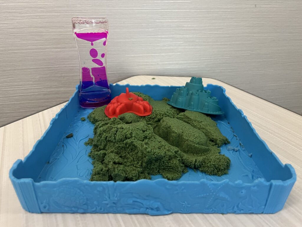 oil timer in a sensory tray with green kinetic sand and molds