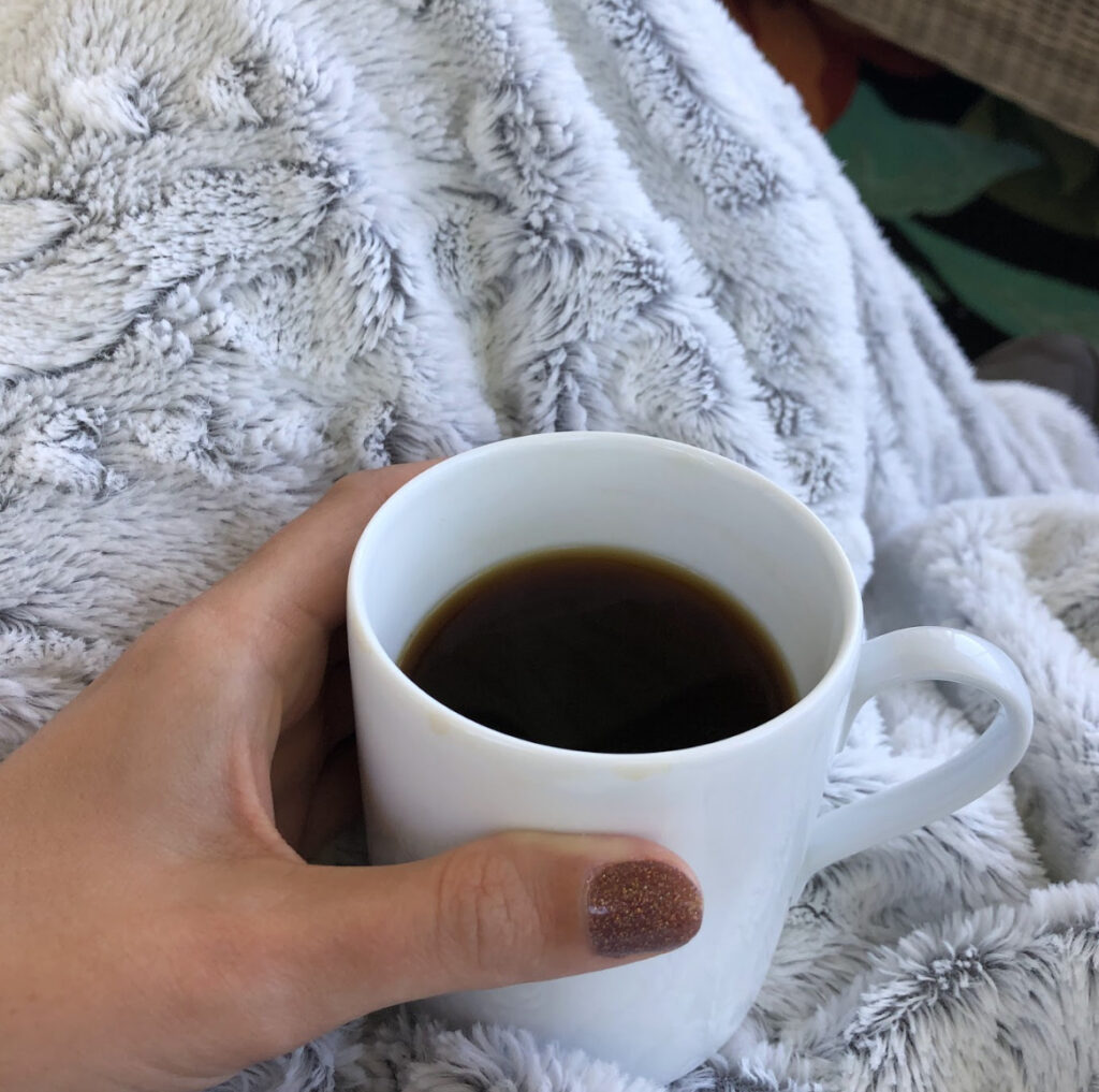 a cup of black coffee on the lap covered with a soft blanket