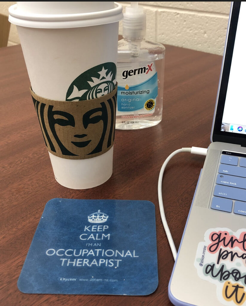 Starbucks cup, hand sanitizer, laptop and a coaster that reads: "keep calm I'm an occupational therapist"