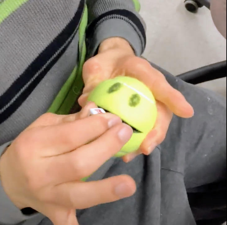student putting letter beads into the "mouth" of a cut tennis ball as a fine motor strength and dexterity activity
