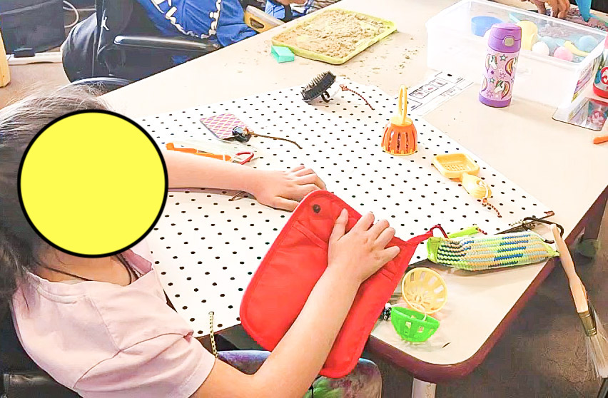 student working on an peg board with objects hanging from it strung with elastic
