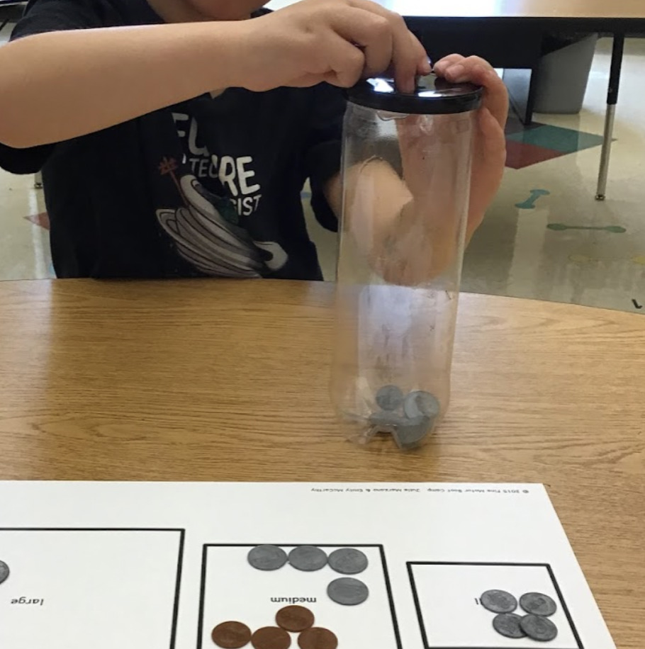 student crossing midline to put coins in a container