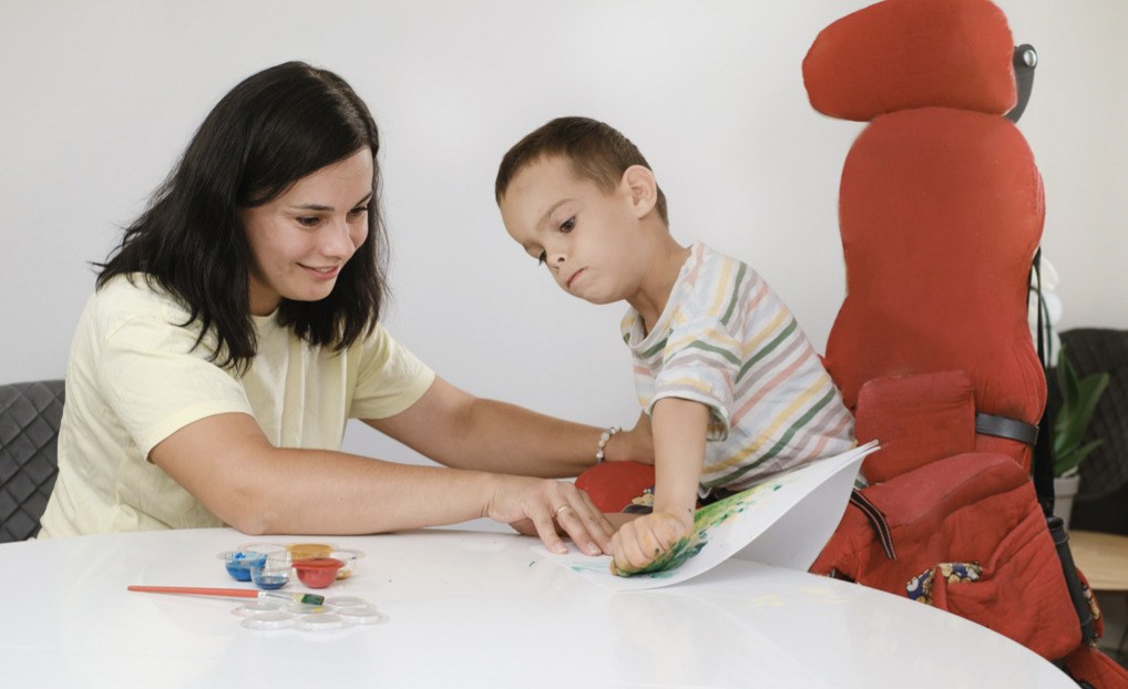 occupational therapist supports a child with physical disabilities paint