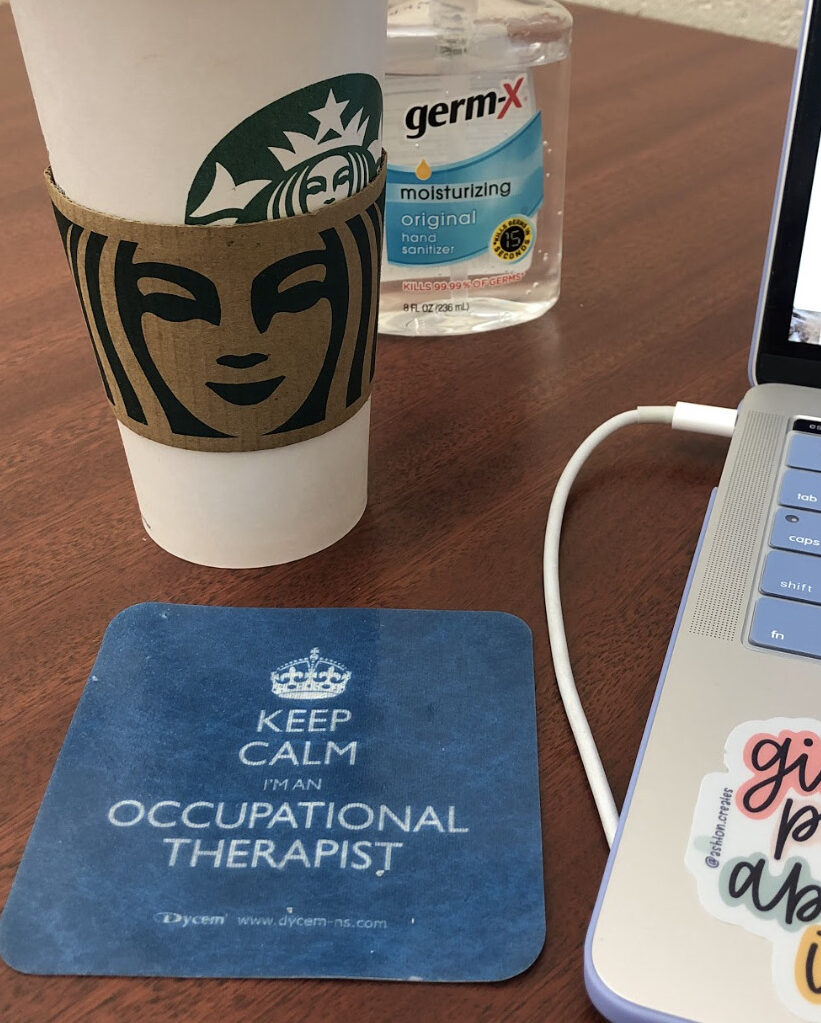 a school desk set up with a Starbucks coffee, Germ-X, a laptop and a coaster that says "keep calm I'm an occupational therapist"