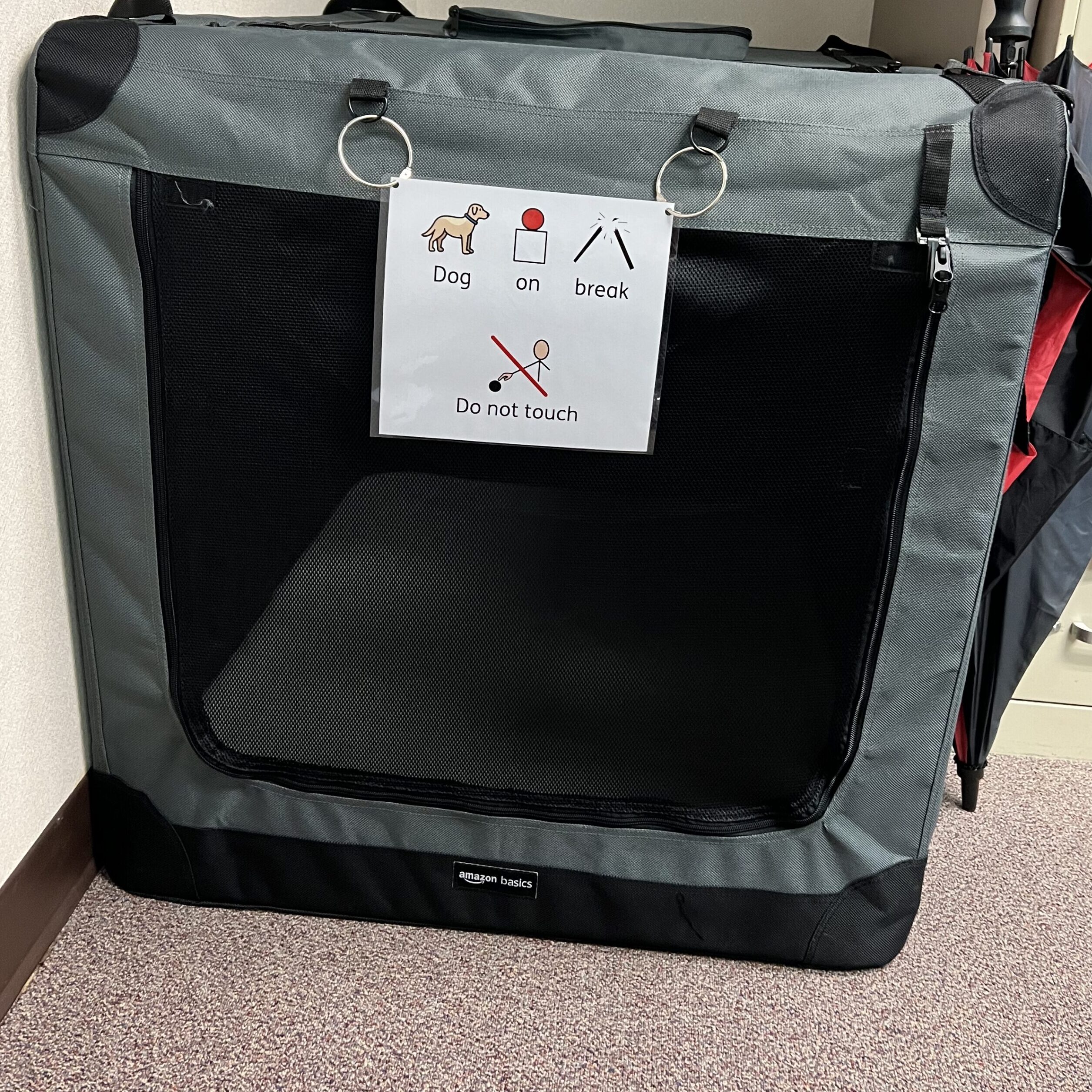 Large Soft kennel with sign hanging on front that states: Dog on break, do not touch. Kennel for service dog in the classroom.