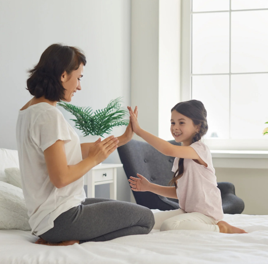 mom and daughter sitting on a bed playing patty cake; high fiving while crossing midline