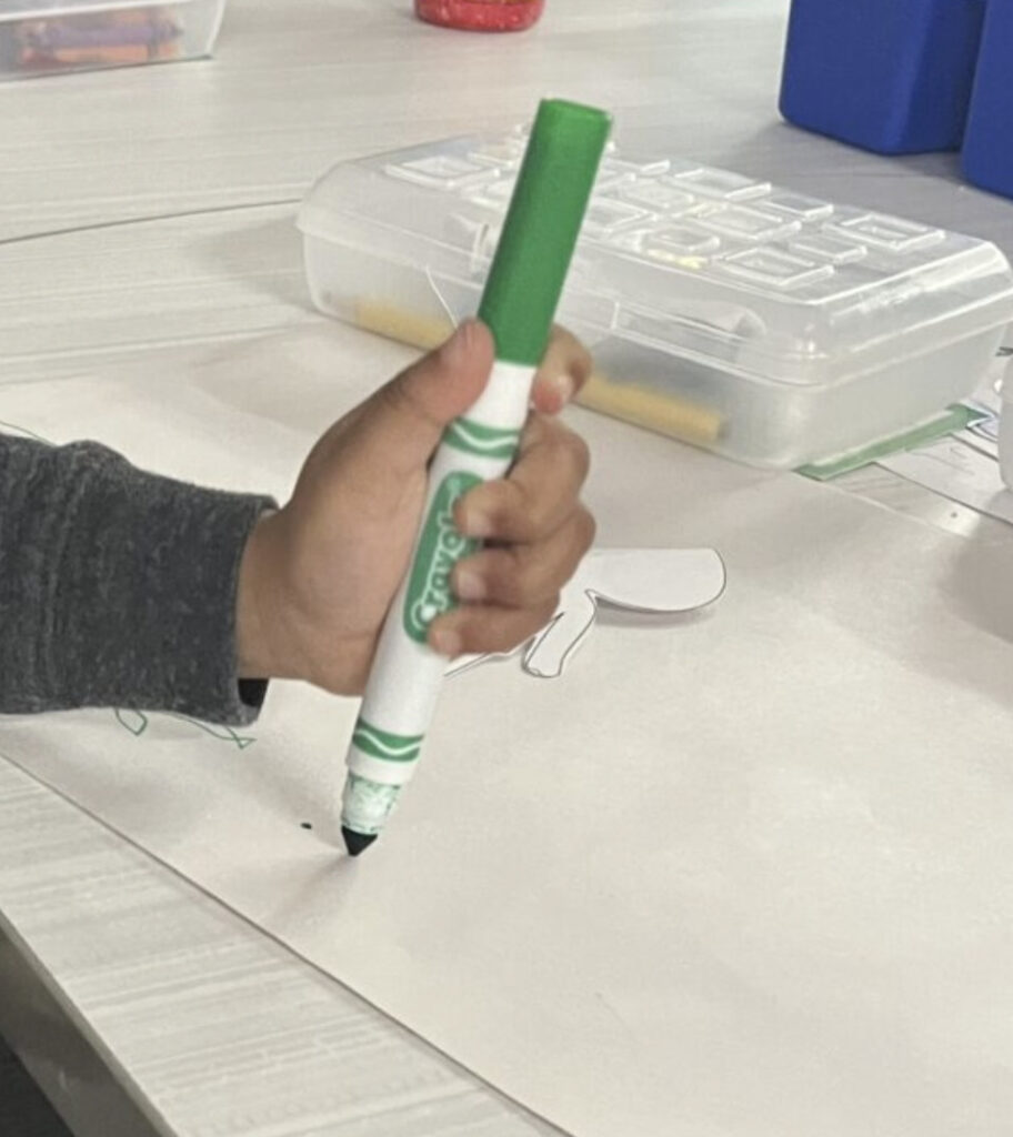 student using a fisted pencil grasp on a green marker with all fingers wrapped around the writing utensil