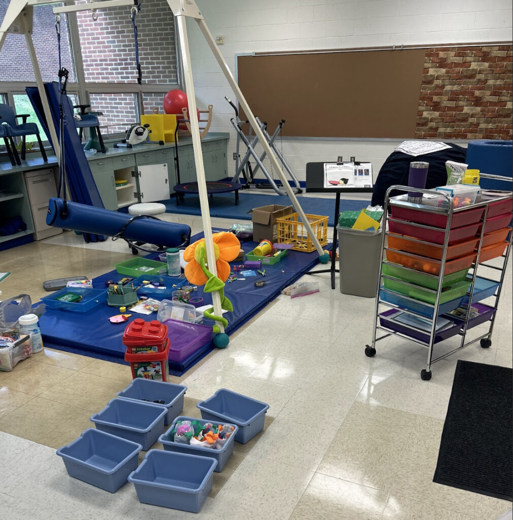 a sensory room during back to school preparation where all the materials are spread out on the floor on a mat under a swing with bins to organize materials