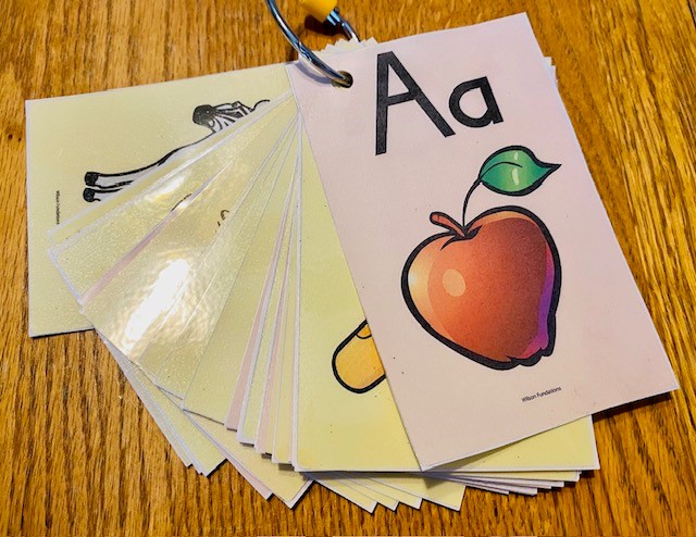 A set of cards on a keyring is shown on a table. The featured card shows the letter A with a red apple underneath.