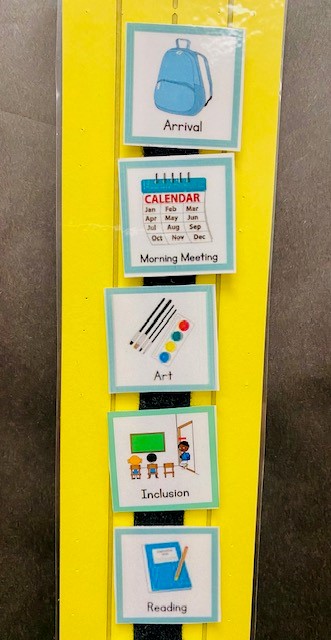 Yellow strip of paper with black Velcro going down the middle. Schedule pictures are shown for arrival, morning meeting, art, inclusion, and reading.