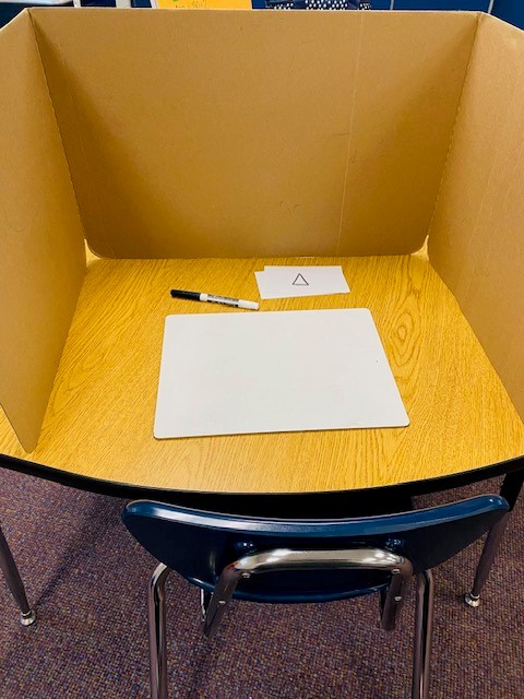 A cardboard privacy folder is on wooden table, surrounding  a whiteboard, marker, and index cards.