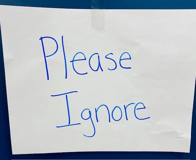 A white piece of paper that says "Please Ignore' is taped to a blue wall.
