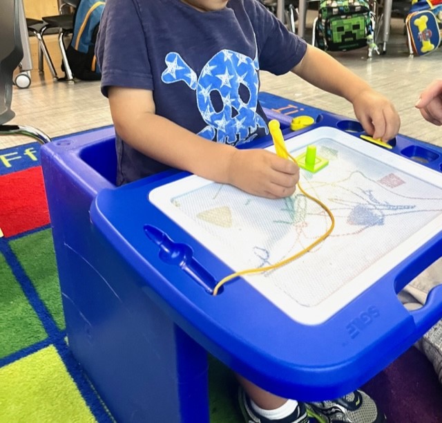 child sitting in cube chair flexible seating drawing on a board as a lap tray
