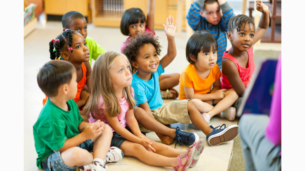 Preschool students in circle time, raising hands to answer questions