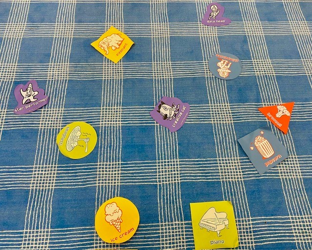 A blue and white carpet with colorful shapes on it. The shapes have symbols from the game "Hullaballoo" such as piano, ice cream, and popcorn.