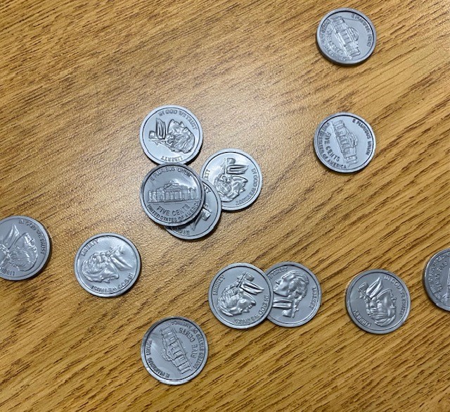 A collection of play nickels is strewn on a wooden table.