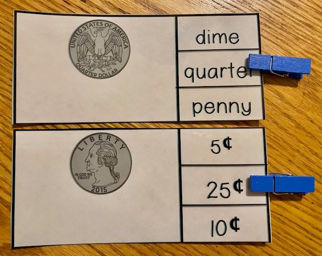 Task box cards are shown on a wooden table. One card shows the back of a quarter, and a clip indicates the word "quarter." The other card shows the front of  quarter, and a clip indicates 25 cents.